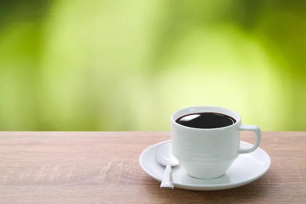 Una taza de café y cuchara en el escritorio de madera con hermoso fondo de naturaleza verde — Foto de Stock