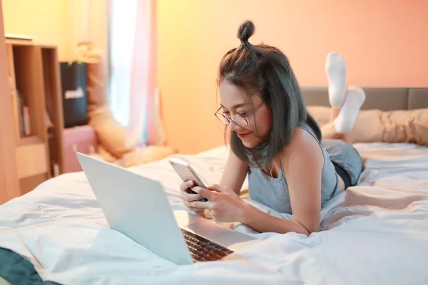 Hermosa y sexy mujer usando ordenador portátil y teléfono celular antes de ir a dormir —  Fotos de Stock