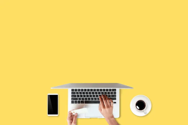 Technology working table with woman hands on laptop computer, credit card, coffee cup and cell phone on yellow background (or shopping and payment online concept) — Stock Photo, Image
