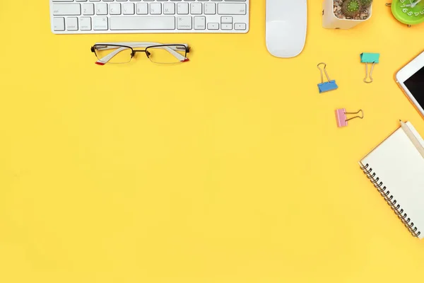 Escritorio de trabajo con computadora, taza de café, cuaderno y vasos sobre fondo pastel amarillo — Foto de Stock