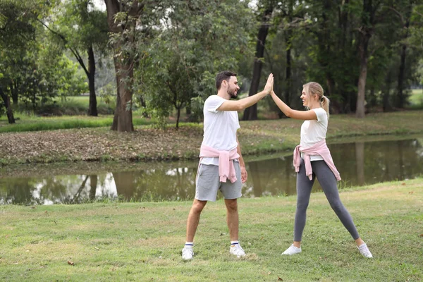 young and healthy couple people enjoying in exercising outdoor and they posting give me five with green trees during summer time in the park