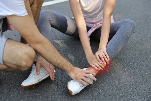 Jovem ajudando mulher corredor que vestindo terno esporte e ferir o tornozelo de muito exercício no parque — Fotografia de Stock