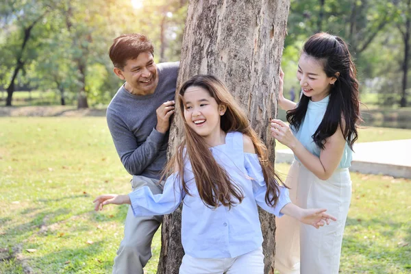 happy family playing tag game or catch up with daughter in the park during summer season with big green trees