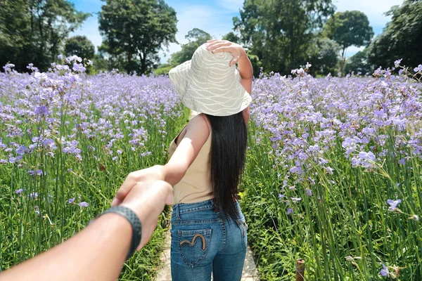 Пара молодых людей, держащихся за руки среди цветочного поля Нага на природе в отпуске и весело проводящих время — стоковое фото