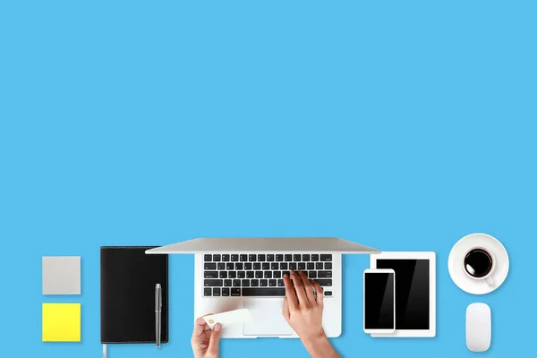 Technology working table with woman hands on laptop computer, credit card, coffee cup and cell phone on blue background (or shopping and payment online concept) — Stock Photo, Image