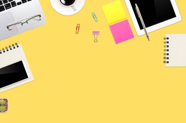 Düz çalışma masası dizüstü bilgisayarı, ofis malzemeleri, kahve fincanı, tablet ve cep telefonu sarı pastel arka planda.