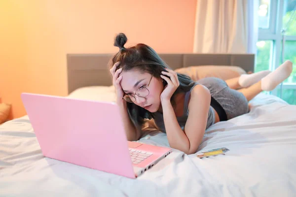 Mujer deprimida y estresada acostada con computadora y tarjeta de crédito en el dormitorio —  Fotos de Stock