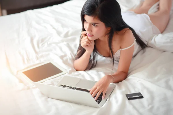 Hermosa y sexy mujer de compras y pago en línea mediante el uso de la computadora y la tableta en el dormitorio con tarjeta de crédito —  Fotos de Stock