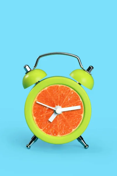 Pomarańczowy zegar na niebieskim pastelowym biurku — Zdjęcie stockowe