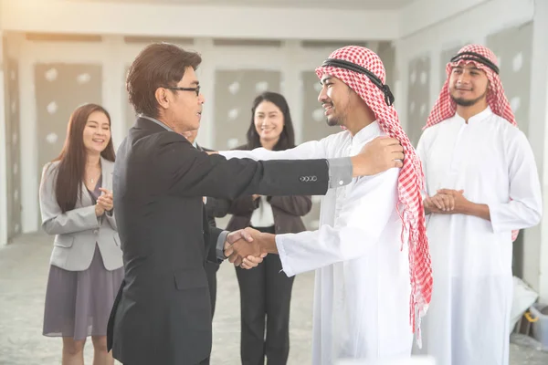 arab saudi businessman hugging with businesspeople for successful deal using as business background (concept of teamwork and partnership)