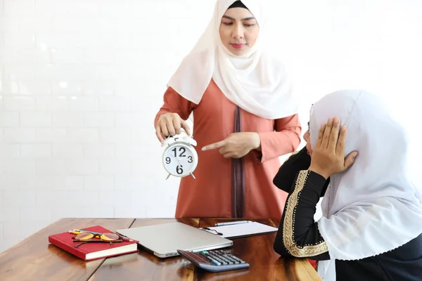 Muslim employee got complaining from her businesswoman muslim boss while showing alarm clock beacause of she working late with computer and coffee cup on wood desk — Stock Photo, Image