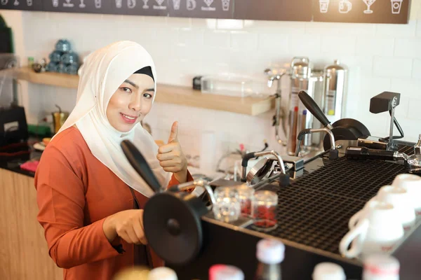 Jovem muçulmano barista menina fazendo café e mostrar polegar para cima significado de sucesso empresarial — Fotografia de Stock