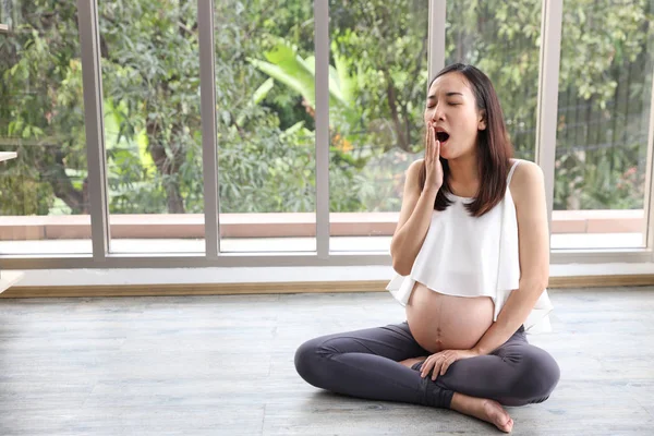 Mladá Asijská těhotná mamka v bílých šatech, která seděla v moderním obývacím pokoji a medituje uvnitř s pózovou pozicí nebo roztáhnutýma a zeleným stromovým pozadím (koncepce zdravotnictví) — Stock fotografie