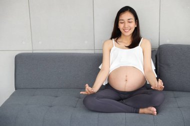 genç hamile kadın oturma odasında oturan ve yoga poz ile kapalı meditasyon keyfi 