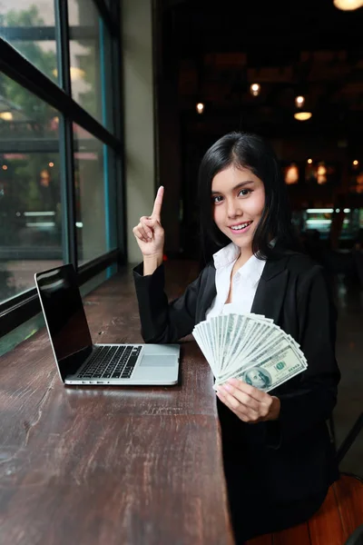 Бізнес-леді показує гроші на руках з комп'ютером на столі — стокове фото
