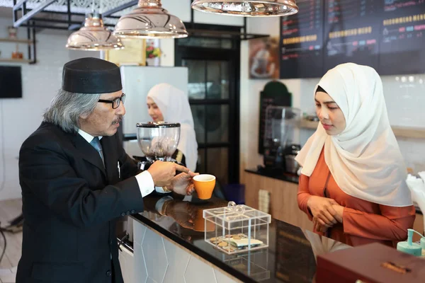 Muslimische Kundin im schwarzen Anzug deutet auf eine Tasse Kaffee und beschwert sich am Schalter mit junger muslimischer Barista-Geschäftsfrau — Stockfoto