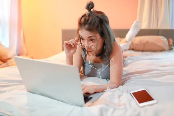 Belle et sexy femme en utilisant un ordinateur portable et en écoutant de la musique de téléphone portable sur le lit — Photo