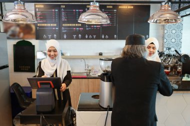 genç müslüman barista kız arka plan ile tezgahta kahve içme siyah takım elbise giyen Müslüman müşteri işadamı nın arka görünümü