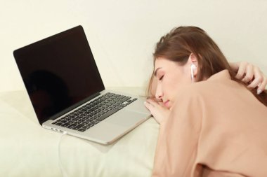 genç kadın bilgisayardan müzik dinlemek ve oturma odasında kanepede uykuya dalmak