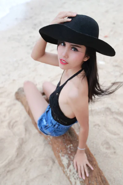 아시아 귀여운 소녀 와 검정 모자 앉아 에 목재 에 the 바닷가 — 스톡 사진