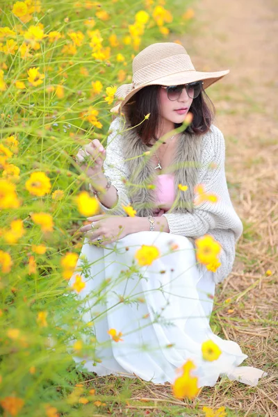 Мила і красива дівчина з капелюхом, що стоїть в природі на відкритому повітрі серед квітів космосу (час відпочинку на концепції відпустки ) — стокове фото