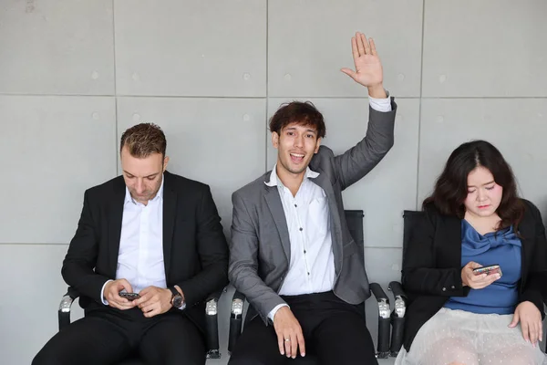 people who line up for HR interview playing smart phone and sitting during waiting and asian business man raising his hand to someone