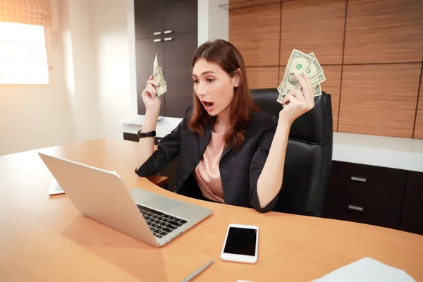 Mooie zakenvrouw portret verrassing en het houden van geld met laptop computer — Stockfoto