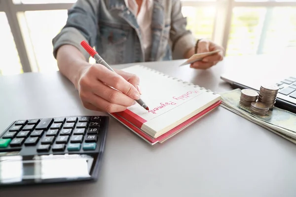 businesswoman writing down monthly payment list on notebook with computer and credit card