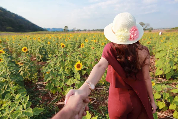 Пара, держащаяся за руки среди подсолнечного поля в природе — стоковое фото