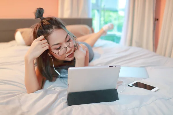 Beautiful and sexy woman using laptop computer and listening to music from tablet on bed — Stock Photo, Image