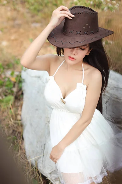 Cute and beautiful girl in white dress sitting in nature outdoors with hat and close her eyes — Stock Photo, Image