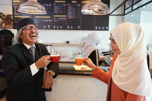 muslim customer businessman wearing black suit drinking coffee at counter with young muslim barista businesswoman background