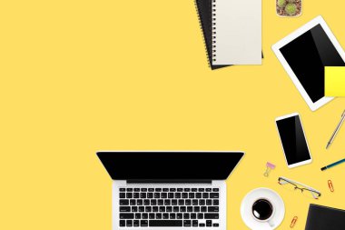Düz çalışma masası dizüstü bilgisayarı, ofis malzemeleri, kahve fincanı, tablet ve cep telefonu sarı pastel arka planda.