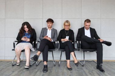 Akıllı telefon oynarken ve beklerken oturan İnsan Kaynakları röportajı için sıraya giren kişiler 