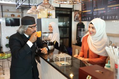 genç müslüman barista kız arka plan ile tezgahta kahve içme siyah takım elbise giyen Müslüman müşteri işadamı