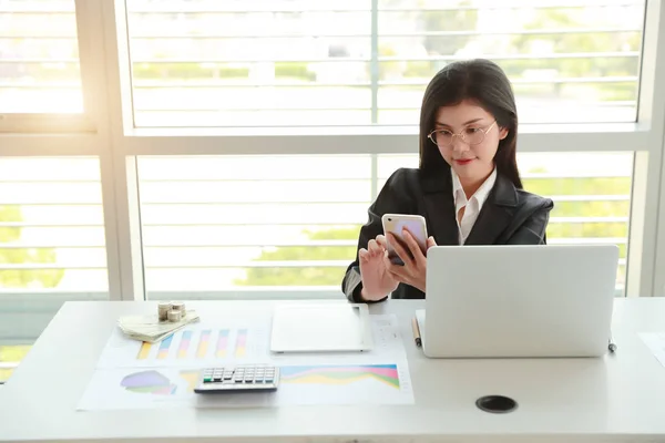 Businesswoman przy użyciu telefonu komórkowego i komputera podczas pracy nad sprawozdaniem podsumowujące firmy z wykresu — Zdjęcie stockowe