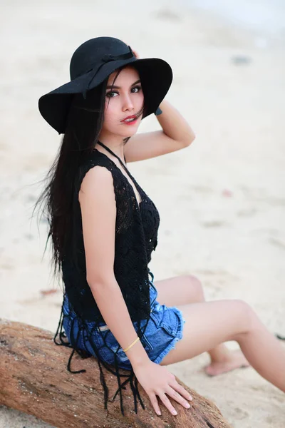 Sahilde ahşap oturan siyah şapkalı asyalı sevimli kız — Stok fotoğraf