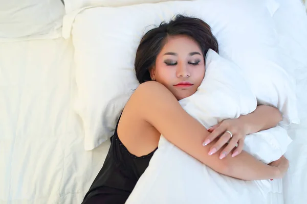 黒いかわいいアジアのモデルは、ベッドの上で眠りと抱擁白い枕を通して見る — ストック写真
