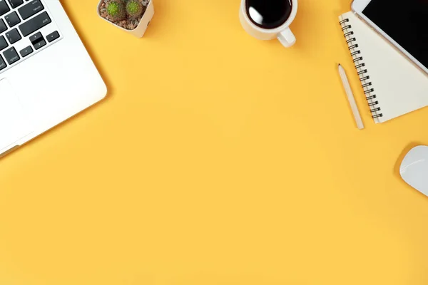 Mesa de trabajo con computadora portátil, suministros de oficina, taza de café, teléfono celular y taza de café sobre fondo amarillo — Foto de Stock