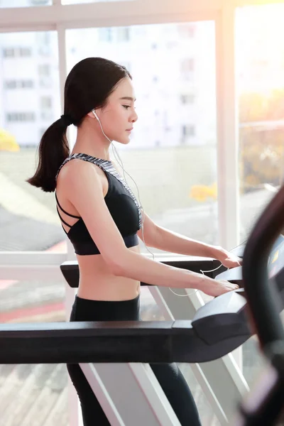 young healthy sport girl walking and listening music on exercise machine in gym (workout concept)