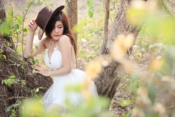Портрет бовдурної азіатки з білим платтям і коричневим капелюхом позують у зеленій природі на відкритому повітрі — стокове фото