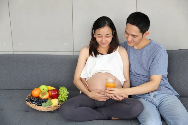 Junge gesunde asiatische schwangere Frau und Ehemann lächeln, während sie ein Glas Orangensaft mit vielen Obstsorten neben sich halten (Gesundheitskonzept)) — Stockfoto