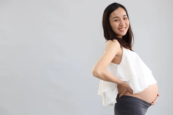 Vista lateral, joven asiática embarazada vientre en vestido blanco con cara sonriente feliz retrato y de pie sobre fondo blanco —  Fotos de Stock