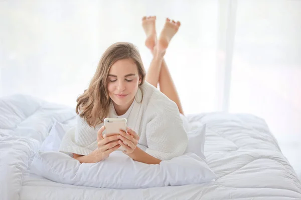 Молода приваблива біла піжама з використанням мобільного телефону на ліжку в спальні (релаксація з концепцією технології ) — стокове фото