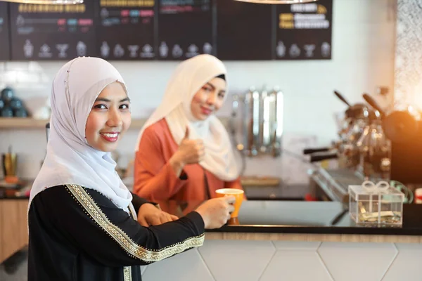 Cliente musulmano bere caffè al bancone con giovane musulmano barista ragazza mostrando pollice su sfondo sfocato — Foto Stock