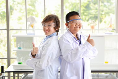 mutlu çocuklar bilim deneyleri yapıyor ve kendilerine güveniyorlar. o başparmak gösteren. (eğitim ve bilim adamı kavramı)