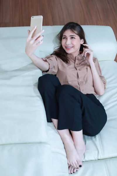 Fiatal nő használ mobiltelefonján, és nem önarckép a nappaliban — Stock Fotó