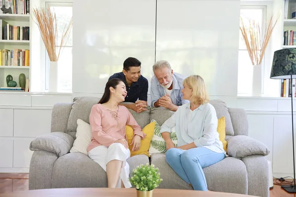 Happy elder multiethnic family meeting and talking on grey sofa in living room with laughing and smiling faces