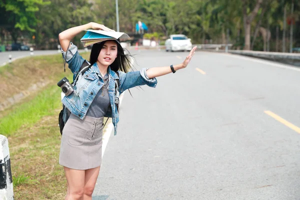 年轻的亚洲旅行者背着背包在公路上等待汽车，而在假期旅行 — 图库照片