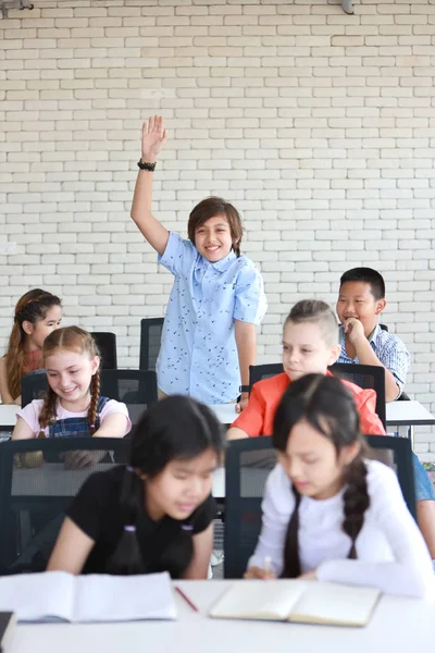 Маленький хлопчик піднімає руки в класі ( концепція освіти ) — стокове фото